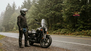Motorcycle rider wearing leather chaps over jeans beside a cruiser in the Pacific Northwest