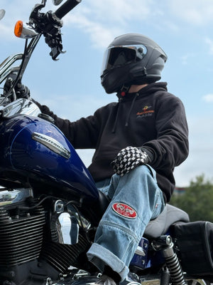 Person sitting on a motorcycle wearing a helmet and checkered gloves with a clear sky background