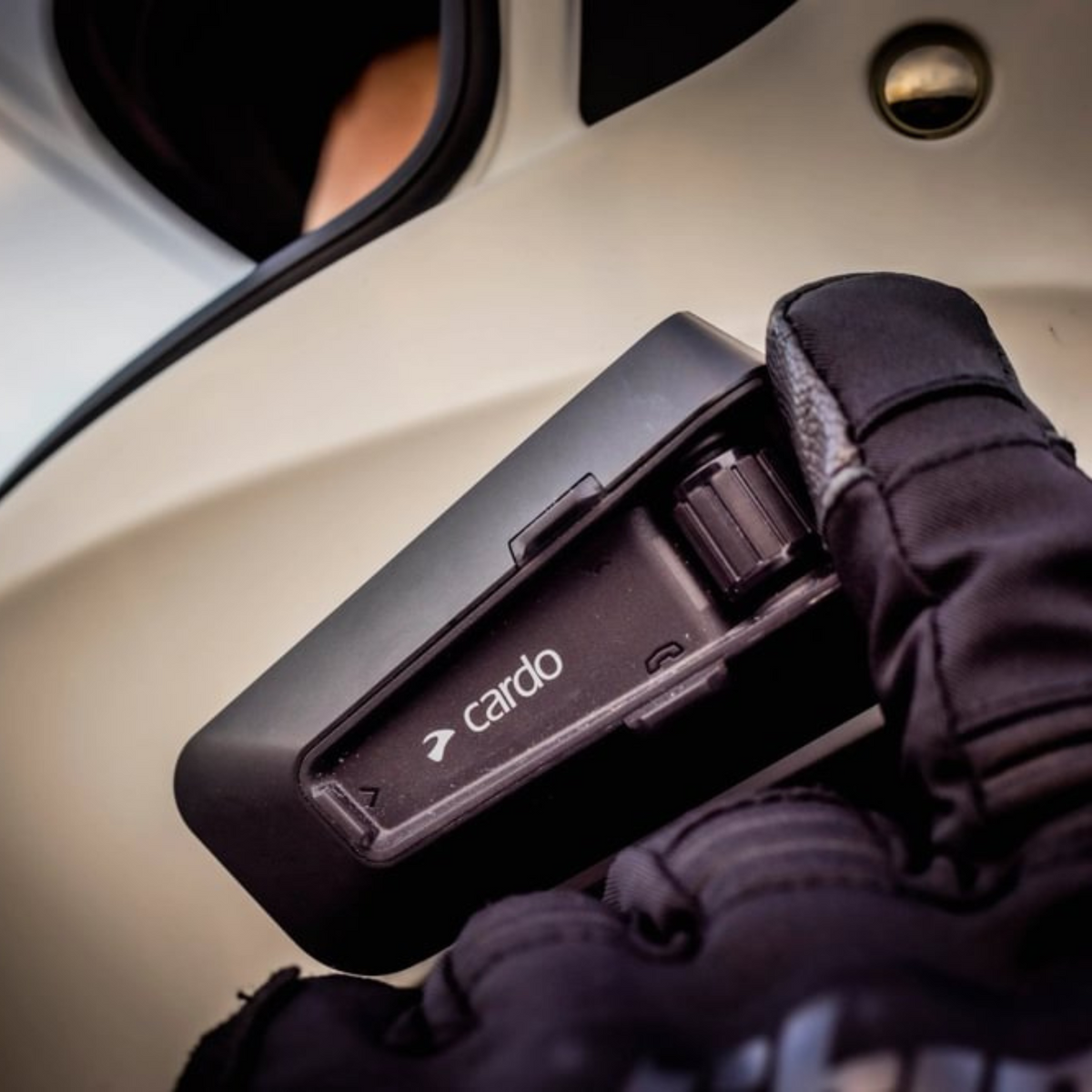 Cardo PACKTALK NEO black communicator mounted on a helmet, gloved hand operating controls