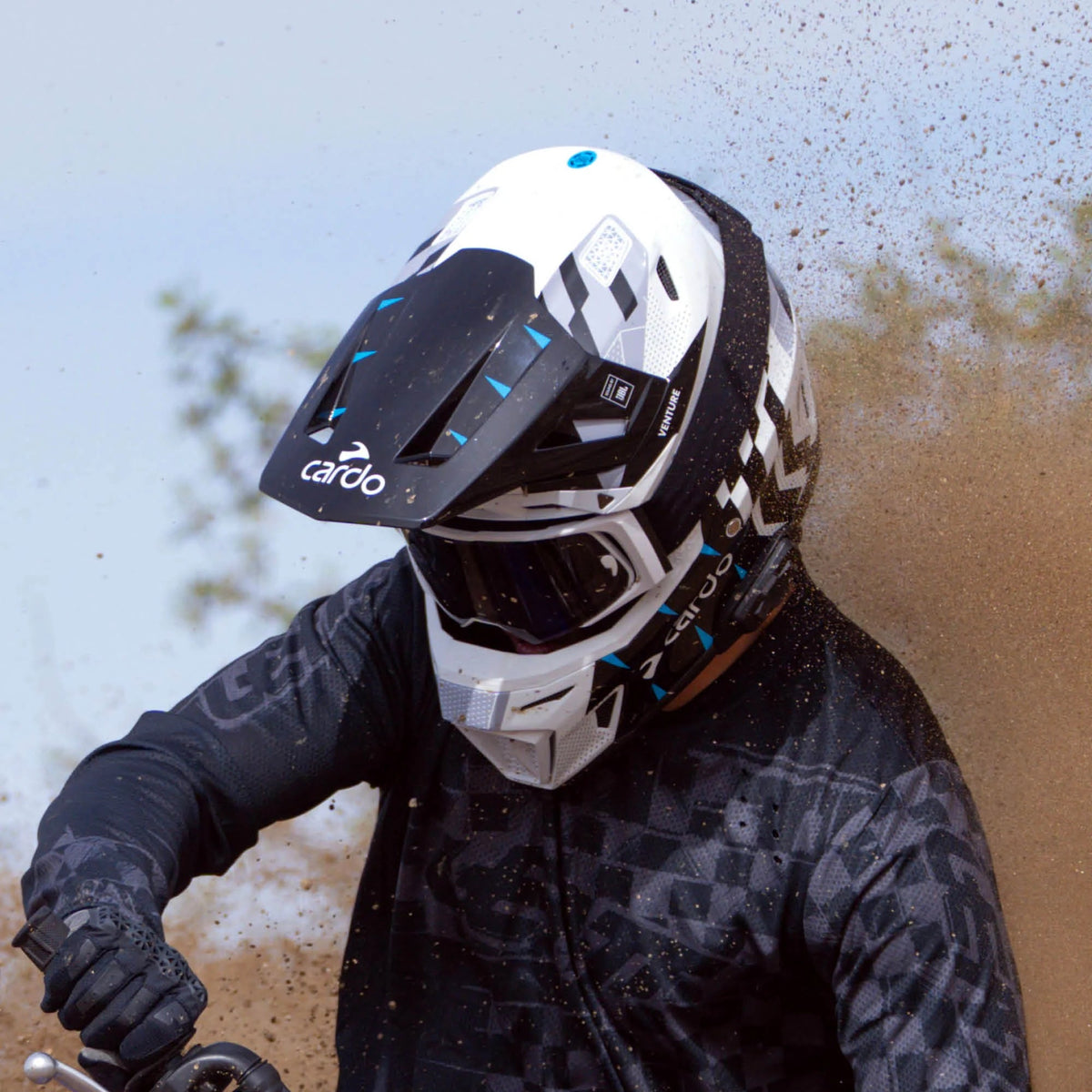 Off-road rider wearing the Cardo VENTURE helmet in dusty conditions