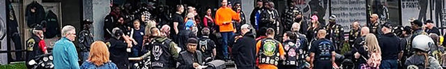 Bikers and motorcycles gathered outside the Eagle Leather store, with the logo and 'Motorcycle Gear & Accessories' sign above. The crowd interacts near the entrance, with motorcycles parked in front.