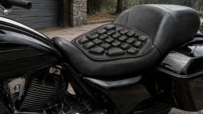 Black inflatable 3D air-cell motorcycle seat cushion with red stitching installed on a black touring motorcycle seat