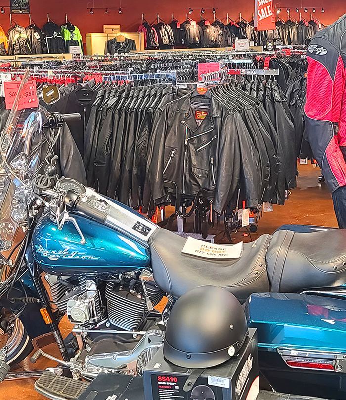 Inside the Eagle Leather store, showcasing racks of men's motorcycle jackets, including black leather and textile options. A blue motorcycle with a windshield is displayed in front of the racks.