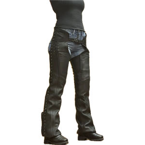 Women's black leather motorcycle chaps with lace-up sides, silver grommets, and adjustable front belt, worn over denim jeans and paired with black boots.